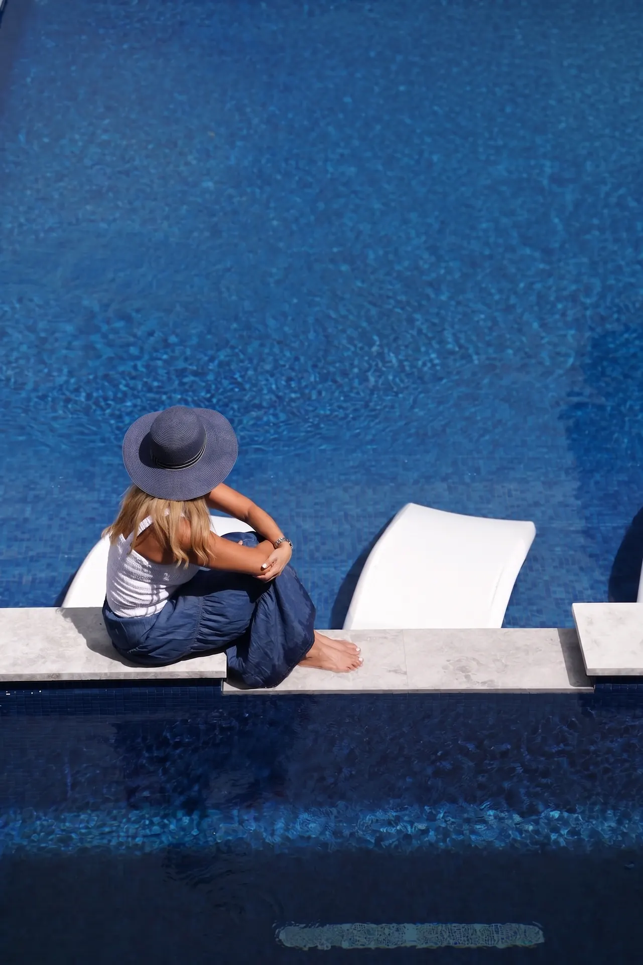 Woman in a navy hat sitting at the edge of a deep blue pool